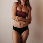 Frau im schwarzen NELLIE Everyday Slip – Vorderansicht, nahtfreie, anschmiegsame Periodenunterwäsche ohne Einschnüren.