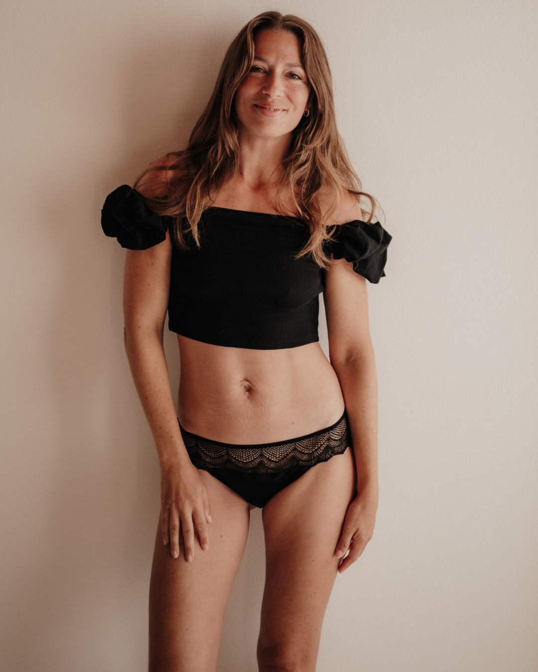 Frau trägt eine schwarze Perioden-Panty im hüftigen Hipster-Style mit extra hoher Sauglage für Frontbleeder. Aus atmungsaktivem TENCEL™ Lyocell, hautfreundlich, mit recycelter Spitze am Bund, fair in Portugal gefertigt.