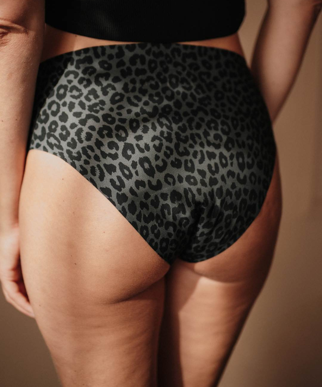 Nahaufnahme einer Frau in nahtloser High-Waist-Periodenunterwäsche im grau-schwarzen Leo-Design, zeigt glatte, weiche Stoffstruktur ohne sichtbare Nähte.