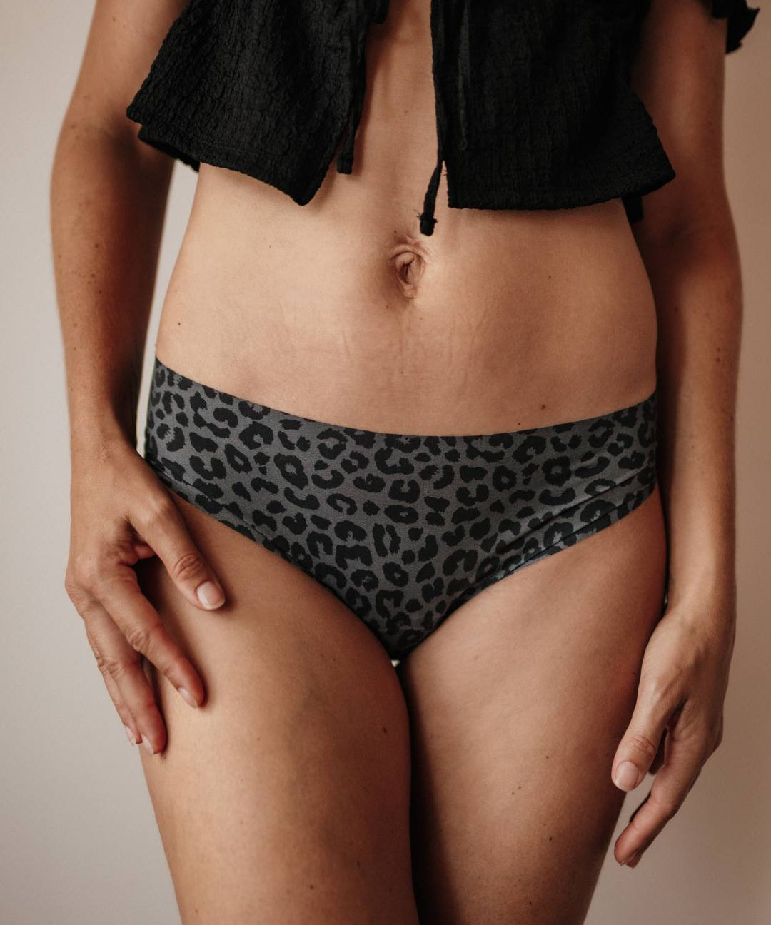 Nahaufnahme einer Frau in Menstruationsunterwäsche mit grau-schwarzem Leo-Muster, zeigt vorderen Bund und weiches, anschmiegsames Material ohne Nähte.