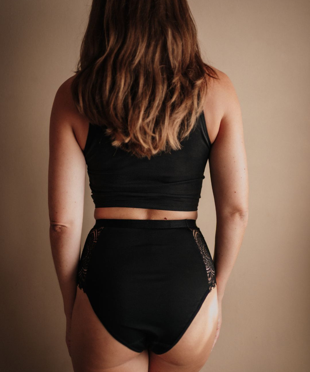 Rückansicht der High Waist Periodenunterwäsche in Schwarz. Der Schnitt bietet eine teilweise Gesäßabdeckung und einen sicheren Sitz an der Taille durch den hohen Bund.